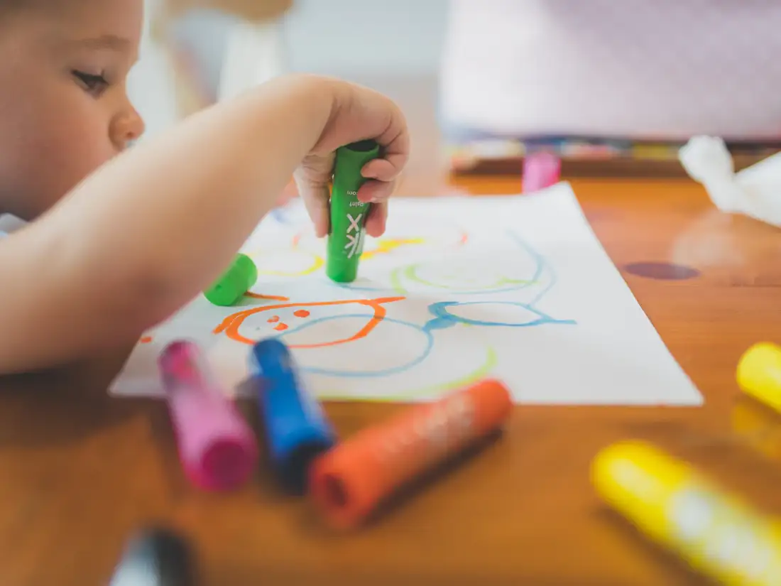 A small child drawing with chunky crayons